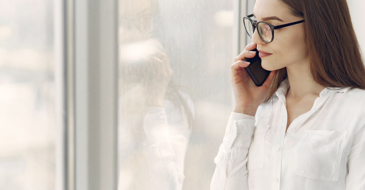 Woman standing at a bright window speaking on a mobile phone