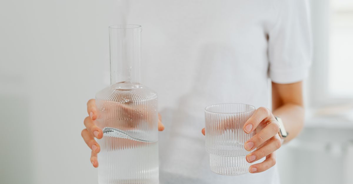 Hands holding a carafe and a glass of water before an egg transfer, filling the bladder