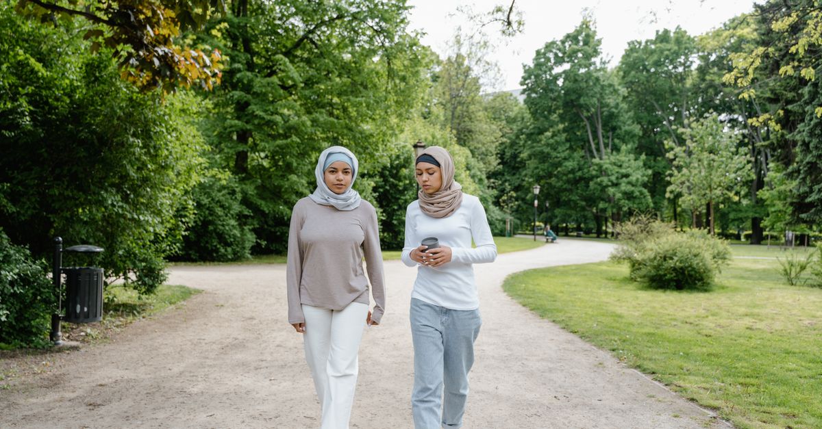 Two women walking together on a park path, talking through a two week wait