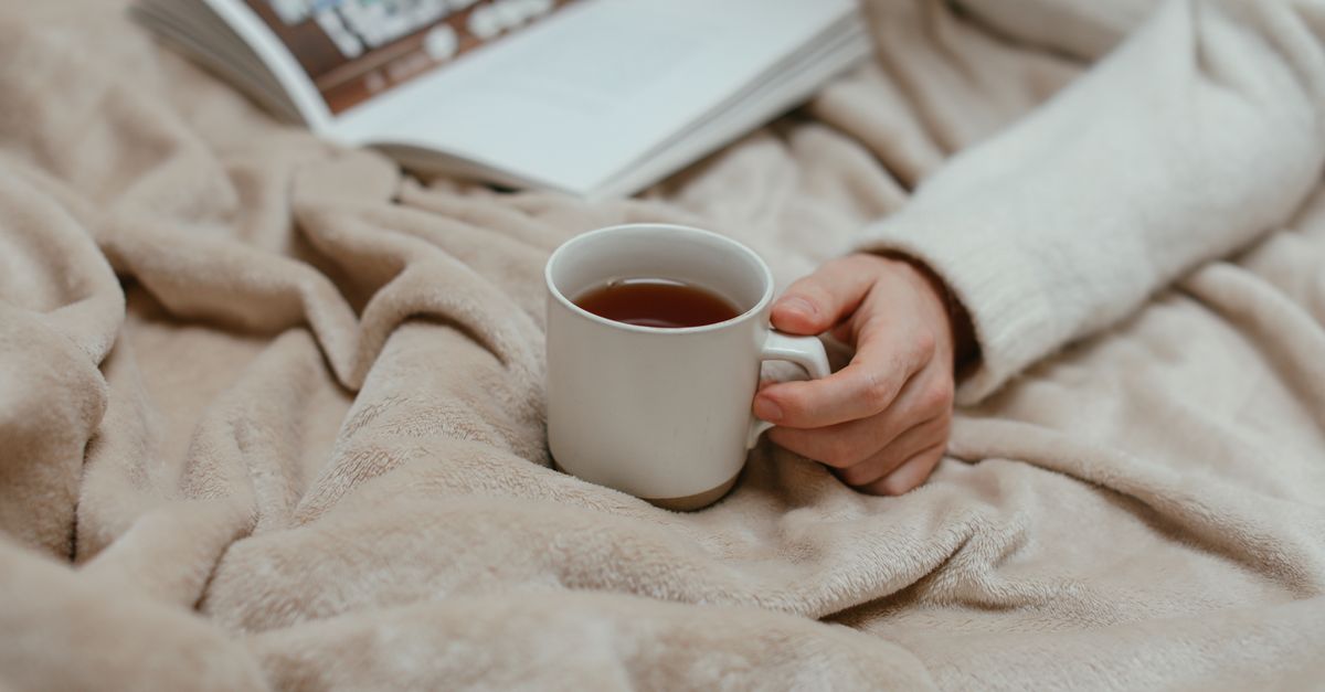 Hand holding a mug on a blanket beside a book while waiting out cramps after embryo transfer