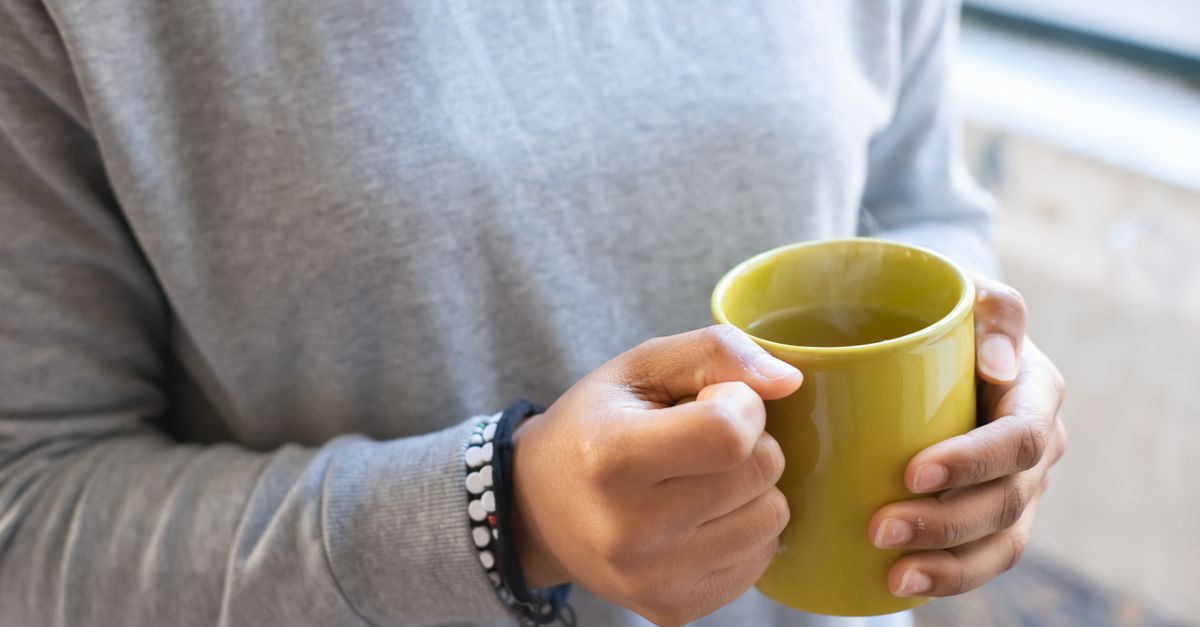 Hands wrapped around a warm mug, comfort while cramping after an egg transfer