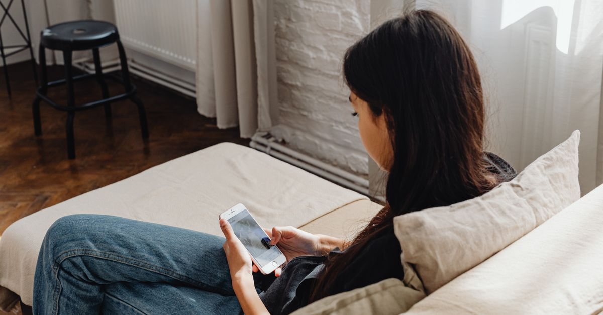 Woman on a sofa holding a phone, waiting for the clinic call about fertilization results
